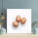 Gracie Oaks Two Brown Egg On White Surface - 1 Piece Square Graphic Art Print On Wrapped Canvas in Brown/White | 12 H x 12 W x 2 D in | Wayfair