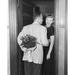 Rear view of mid adult man standing with mid adult woman at doorway hiding bouquet of flowers behind back Poster Print (24 x 36)