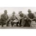 Group portrait of a woman and three men crouched outside smiling; one of the men is displaying a dish of panned gold Poster Print (24 x 36)