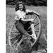 Young Woman Sitting on a Wagon Wheel & Smiling Poster Print - 18 x 24 in.